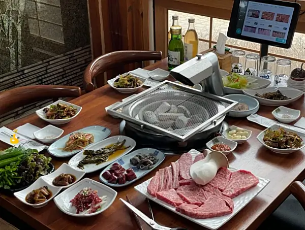 테이블 위에 4인상이 차려져 있고, 가운데 숯불 화로가 있는 고기집 사진