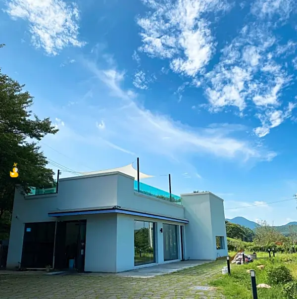파란 하늘 아래 초록색 잔디밭 사이에 단층짜리 하얀 카페 건물이 서 있는 모습