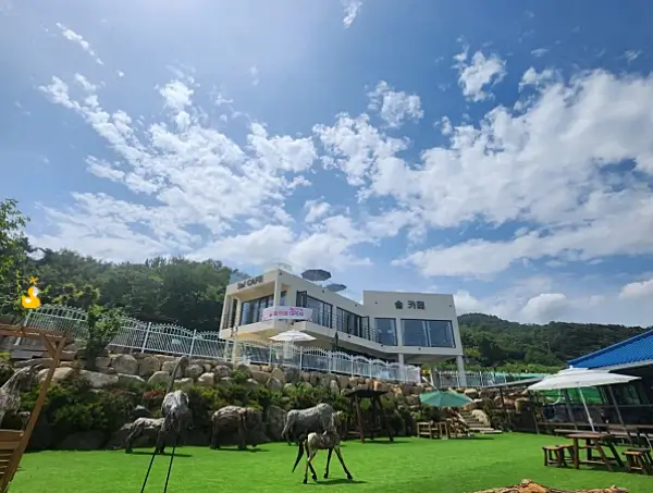 높고 푸른 하늘 아래 짙은 초록 잔디 밭 위엔 다양한 동물 조형물이 있고, 그 위로 하얀 2층짜리 솔 카페 건물이 있는 사진