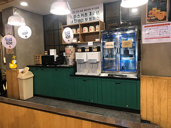 성심당 테라스키친 셀프바에 장국 디스펜서, 정수기, 전자렌지, 컵과 장국 그릇 등이 놓여 있는 모습