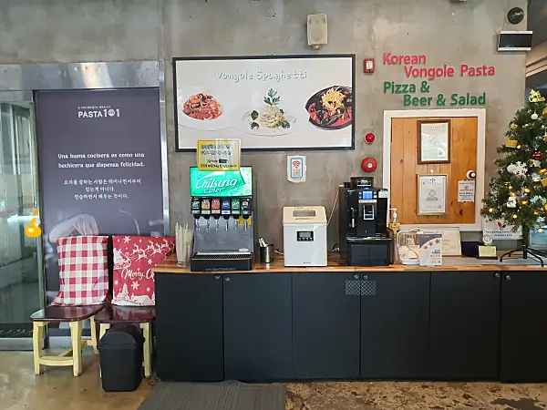 탄산음료 기계와 제빙기, 커피머신이 놓여 있는 테이블과 그 옆에 놓인 대기용 의자