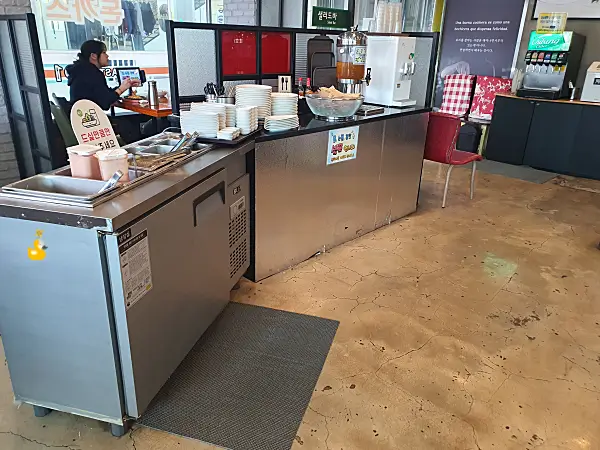 자스민차와 정수기, 밑접시와 샐러드 등이 마련되어 있는 셀프바와 그 옆 테이블에서 식사하는 사람