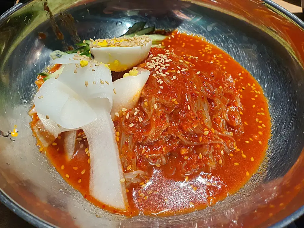 삶은 달걀 반쪽에 무절임과 오이채가 올라가 있는 담가화로구이 무거점 비빔냉면