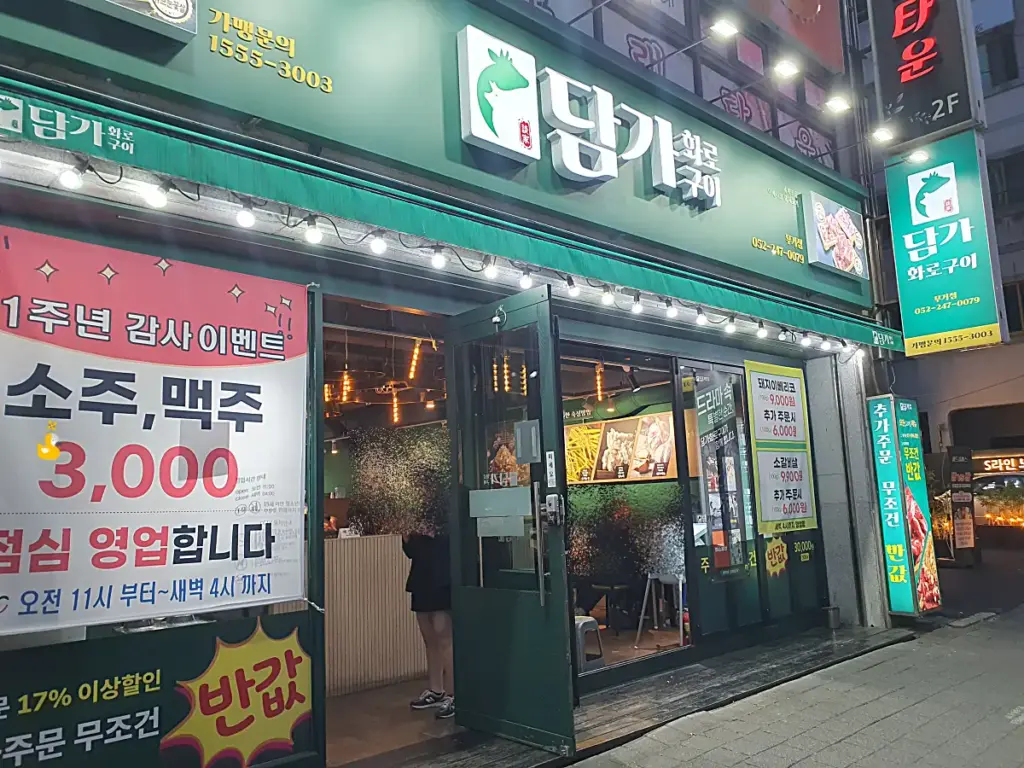 담가화로구이 무거점의 녹색 간판과 다양한 이벤트 현수막이 벽에 걸려 있는 모습