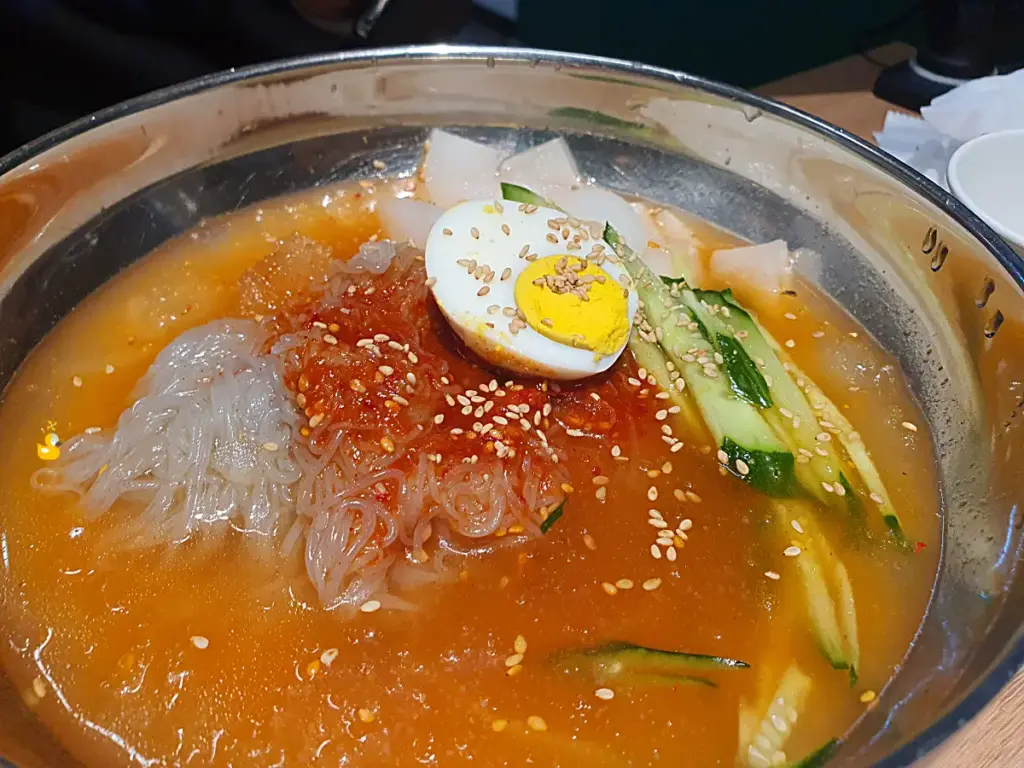 삶은 달걀 반쪽과 오이채, 무절임이 올려진 담가화로구이 무거점 물냉면