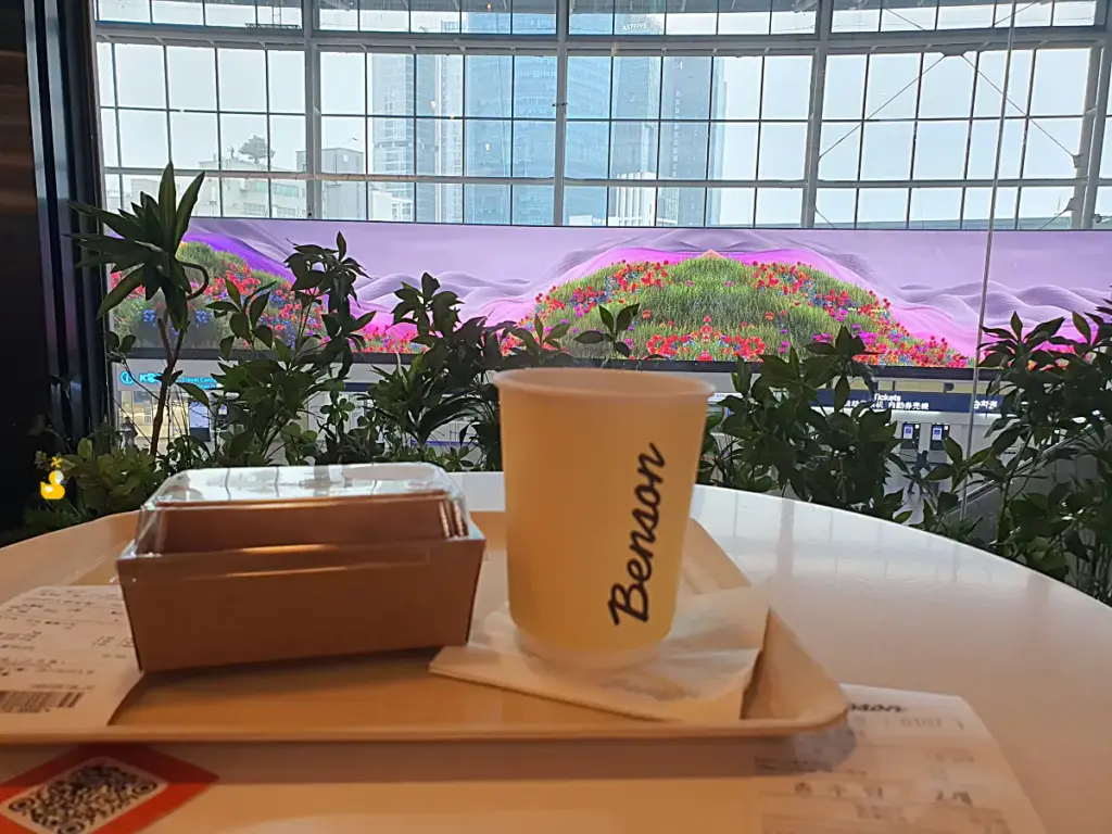 벤슨 서울역점 전광판이 내려다보이는 테이블과 샌드위치, 커피 한 잔