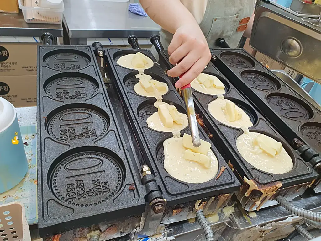 경주 십원빵 가게에서 직원이 십원빵 반죽에 치즈를 올리는 모습