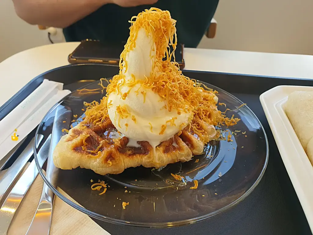 크로플 위에 바닐라아이스크림, 그 위에 브라운 치즈와 꿀이 뿌려져 있는 모습